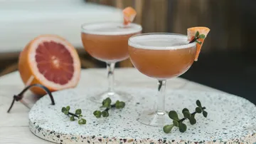 Zwei Cocktails stehen auf einem Marmorbrett, umgeben von Früchten.