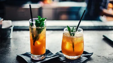 Zwei Cocktails stehen auf einer Bar, dekoriert mit Kräutern.