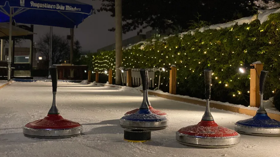 Curling stones on snowy outdoor lane with lights.