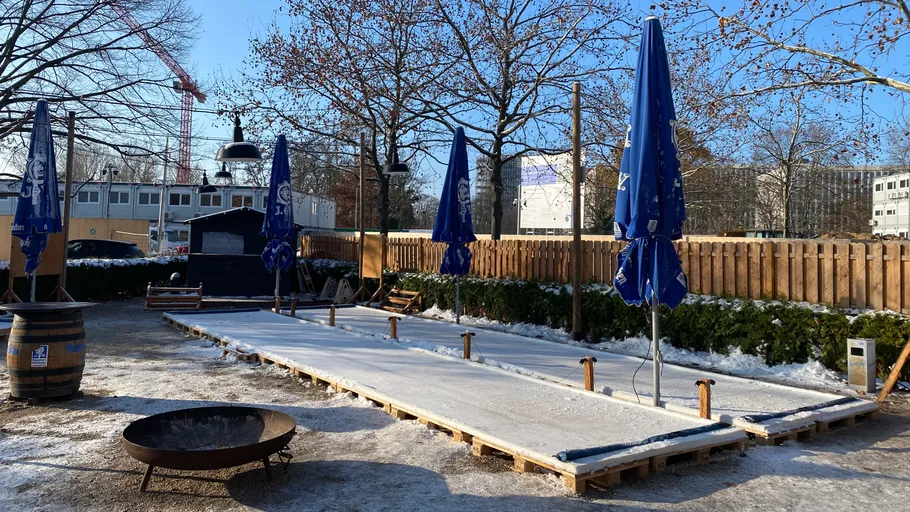 Eisstockbahn im Freien mit blauen Sonnenschirmen.