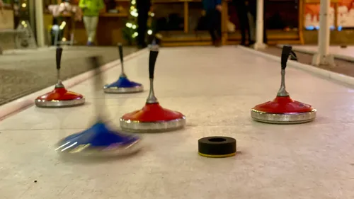 Curling stones sliding on ice sheet indoors.