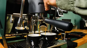 Espresso machine brews coffee in two cups on a wooden plate.