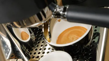 Espresso machine brews coffee in a black cup in a kitchen environment.