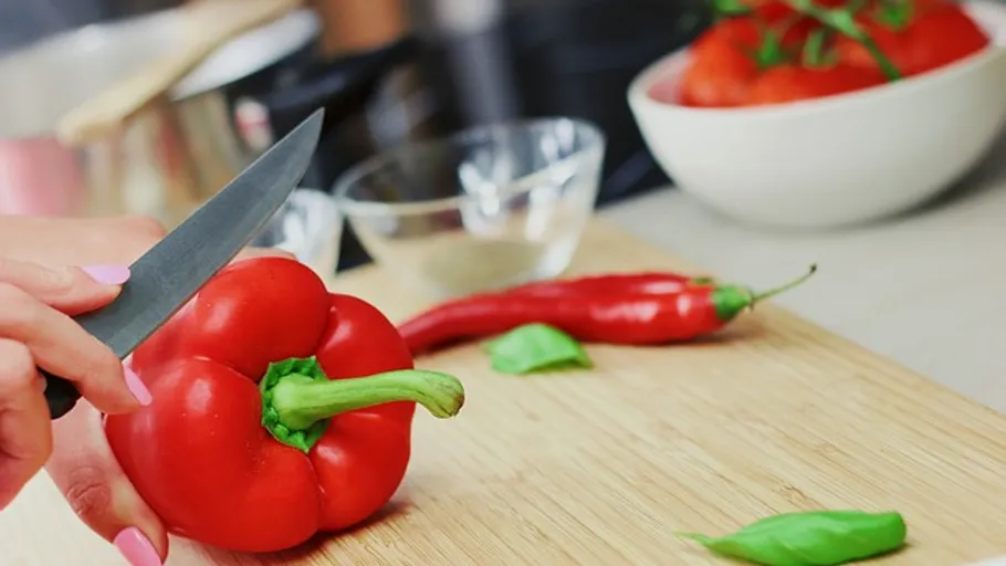 Red peppers are cut on a wooden board, surrounded by ingredients.
