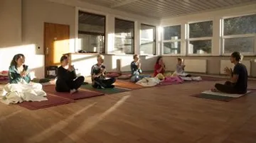 People sit cross-legged and meditate in a room.