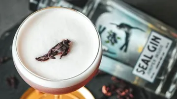 Cocktail mit Schaumhaube und Blüten auf einem Tisch.