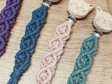 Colourful pacifier chains made of braided thread on a wooden background.