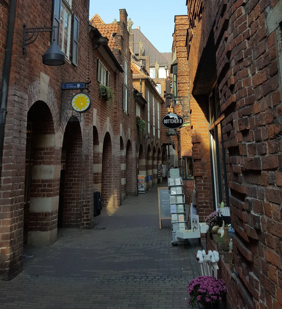 Enge Gasse mit Backsteinmauern, Geschäften und Pflanzen.