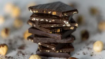 Stack of dark chocolate is surrounded by nuts.