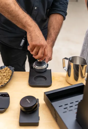 Man presses coffee powder in a machine on a table.
