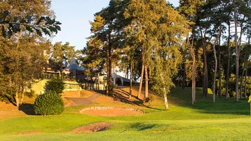 Green golf course with trees and a building in the background.