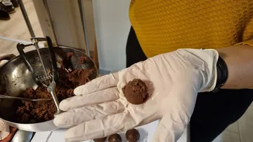 One hand holds chocolate ball dough in rubber gloves.