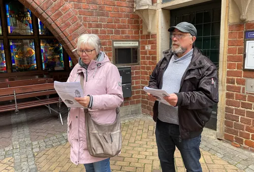 Zwei Personen lesen Informationen vor einer Backsteinmauer.