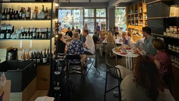 Wine rack with bottles, diners eating and drinking in a restaurant.