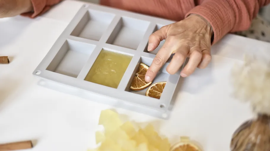 Silikonform mit einer Hand, die getrocknete Orangenscheiben hinzufügt.