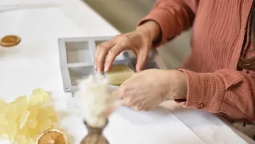 Hand greift Seife und platziert sie in Form auf Tisch.