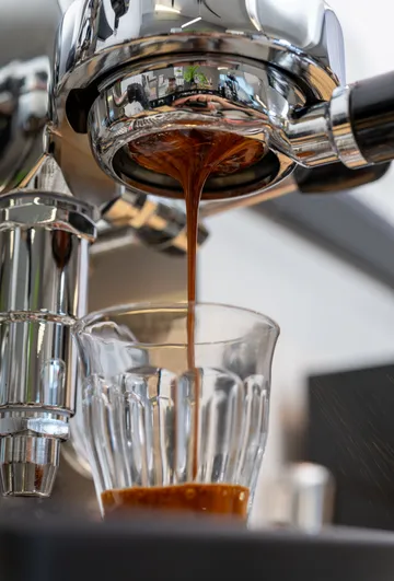 Kaffeetropfen fließen in ein Glas unter einer Maschine.