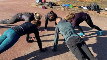 Six people do push-ups on a sports field.
