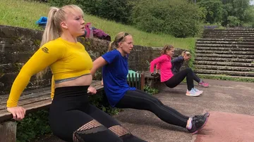 Four women work out with dips on an outdoor bench.