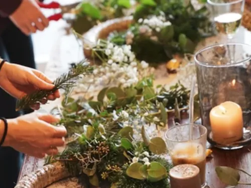 Hands make a wreath with fresh plants and candles.