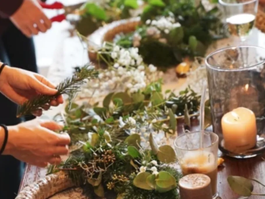 Hands make a wreath with fresh plants and candles.