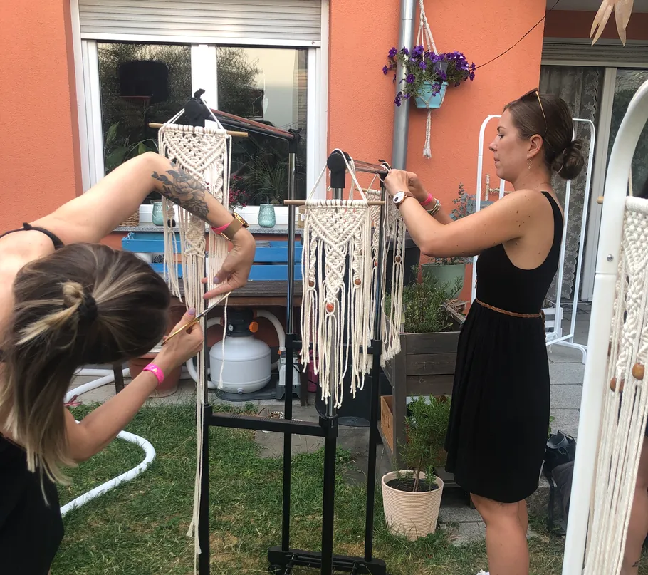 Zwei Frauen schneiden Makramee-Dekoration in einem Garten.