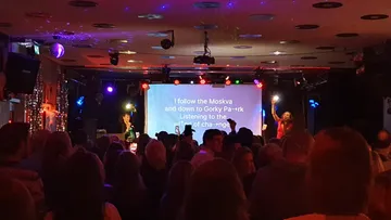 Die Menge schaut sich eine Karaoke-Aufführung in einer schwach beleuchteten Bar an.