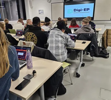 Students use laptops in a classroom with a presentation.