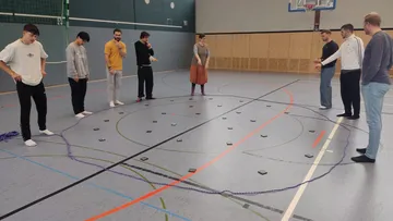 Group participants stand around a circular floor with objects.
