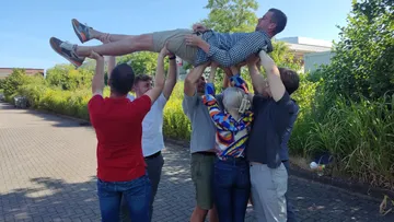 Gruppierung hebt einen Mann in der Luft, sonniger Platz.
