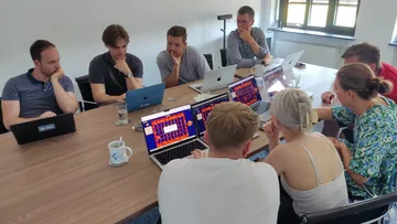 Gruppe von Menschen arbeitet an Laptops an einem Tisch.