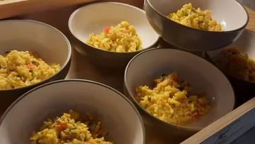 Six bowls of yellow rice on a wooden table.