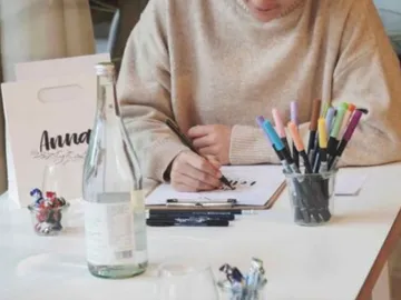 Person writes with pen on a clipboard at the table.