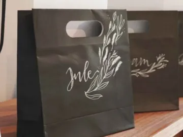 Black paper bag is on a table, labeled.