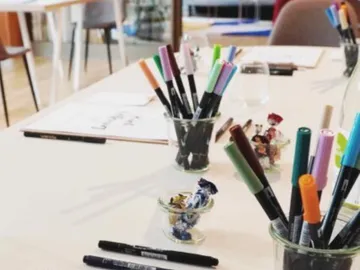 Colourful markers stand in glasses on a table.