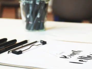 Write on paper with pens and a glass in the background.