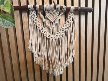 Makramee-Wandbehang hängt an einem Holzstamm vor Holzpaneelen.