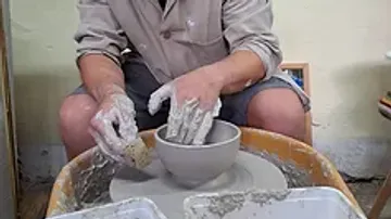 Potter uses hands to form a bowl on a potter's wheel.