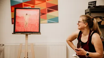 A woman smiles in front of a painting in a room.