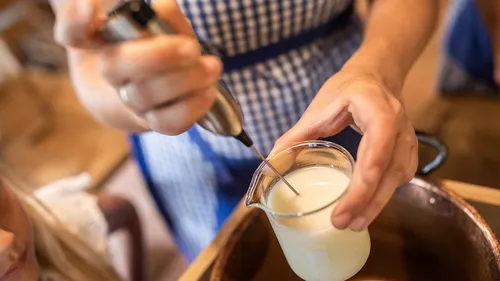 Eine Person schäumt Milch in einem Becher. Umgebung ist eine Küche.