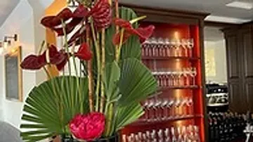 Blumenarrangement steht vor einer Bar mit Gläsern.