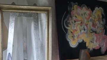 A golden mirror reflects a colorful painting.