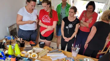 Six women look at material at the table in a workshop.