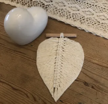Weißes Herz und geflochtenes Blatt auf Holztisch.