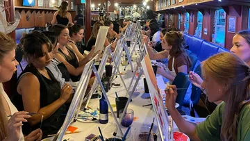Women paint on canvases in a cozy restaurant.