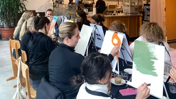 Frauen malen gemeinsam auf Leinwänden in einem Café.