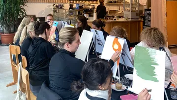 Menschen malen auf Leinwänden in einem Café-Umfeld.