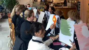 Women paint on easels in a cafe.