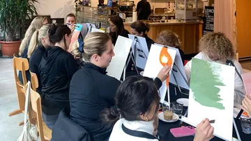 Women paint on canvases in a cafe.
