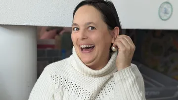 Frau mit Pullover lächelt und trägt Ohrringe in Wohnzimmer.